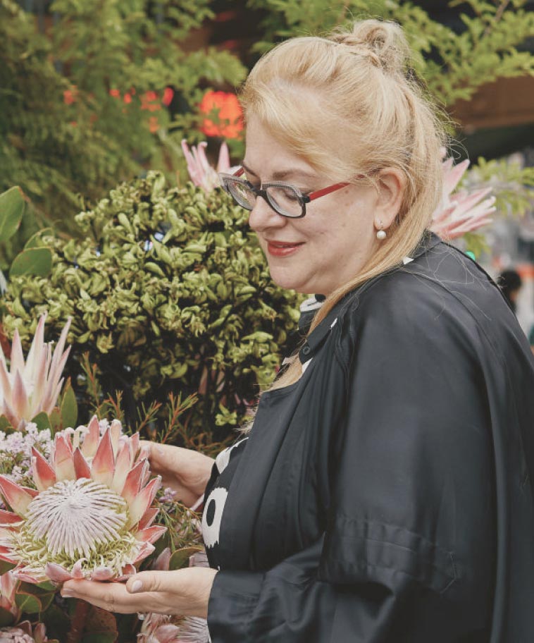 This photograph depicts Cherrie Miriklis, the founder of Flowers Vasette. She is holding a large pink protea flower.