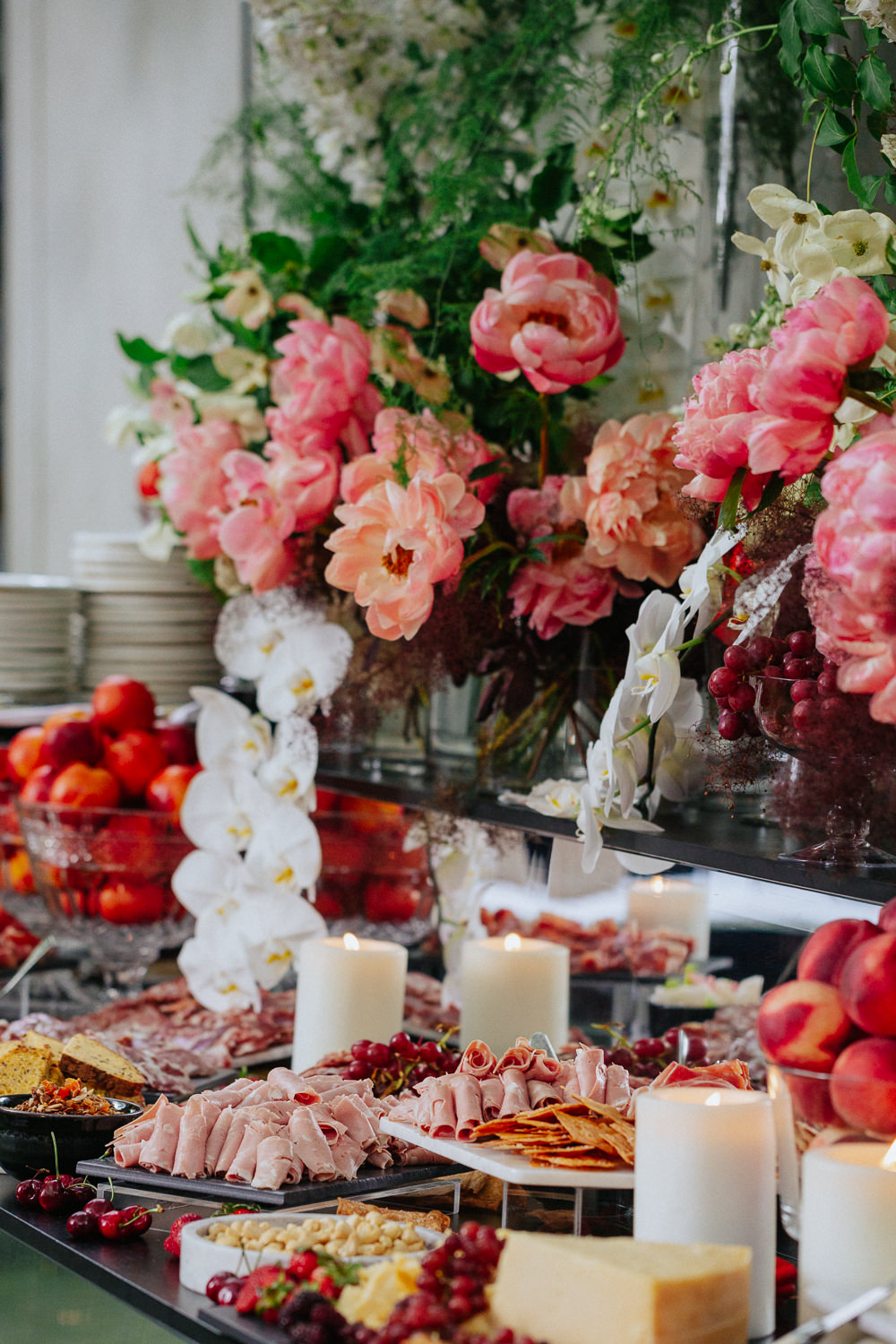 A buffet of food in front of a table of pink and white flowers.