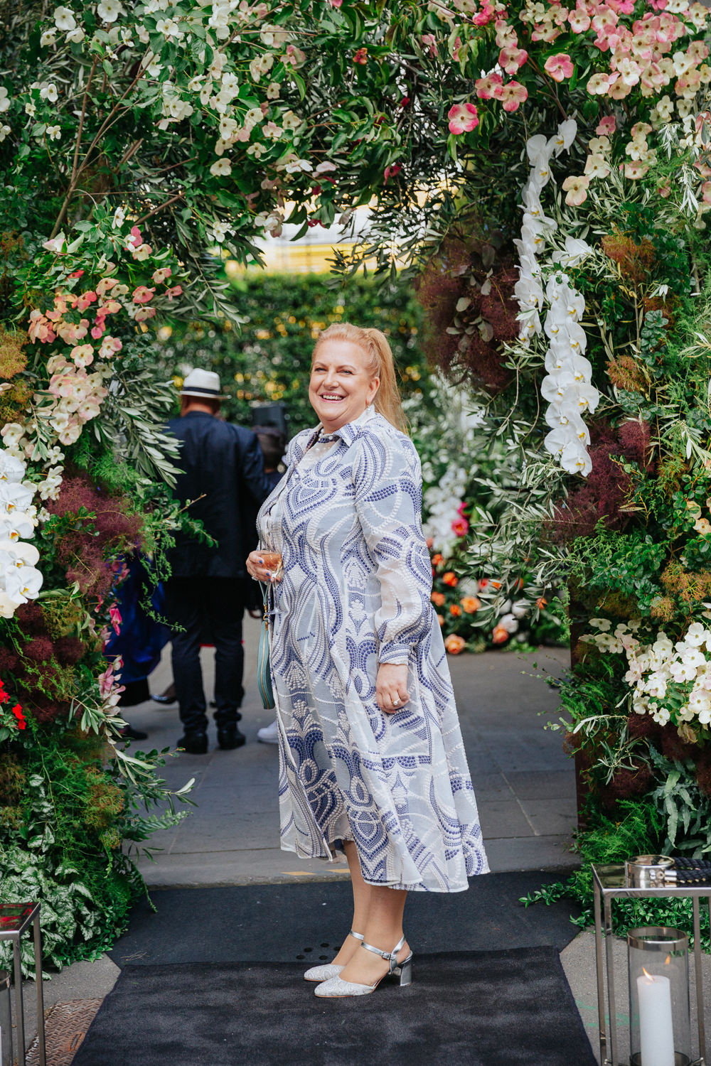 CEO of Flowers Vasette, Cherrie Miriklis, standing within a pink, green and white floral archway.