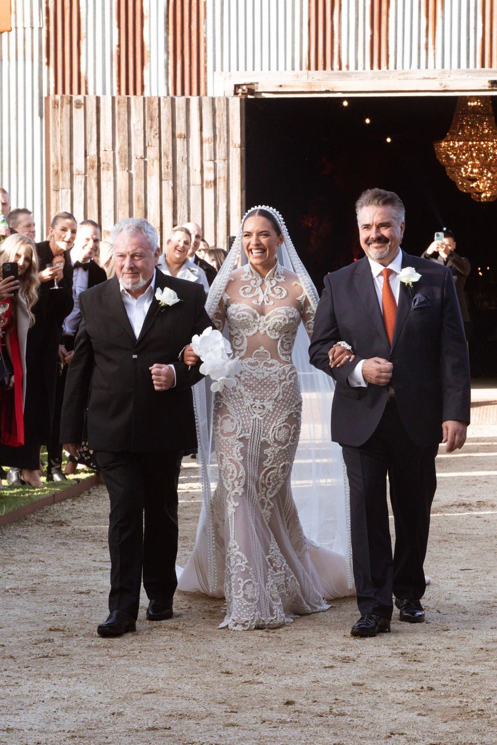 This photo depicts Olympia Valance walking down the aisle at her wedding. She is holding a white phalaenopsis orchid.