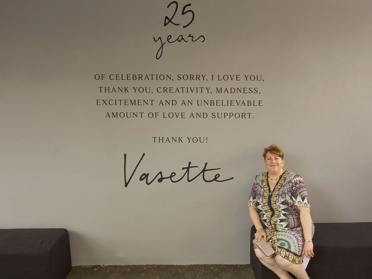 Flowers Vasette founder Cherrie Miriklis, sits in front of a wall mural. The mural reads: 25 years of celebration, sorry, I love you, thank you, creativity, madness, excitement and an unbelievable amount of love and support. Thank you! Vasette.