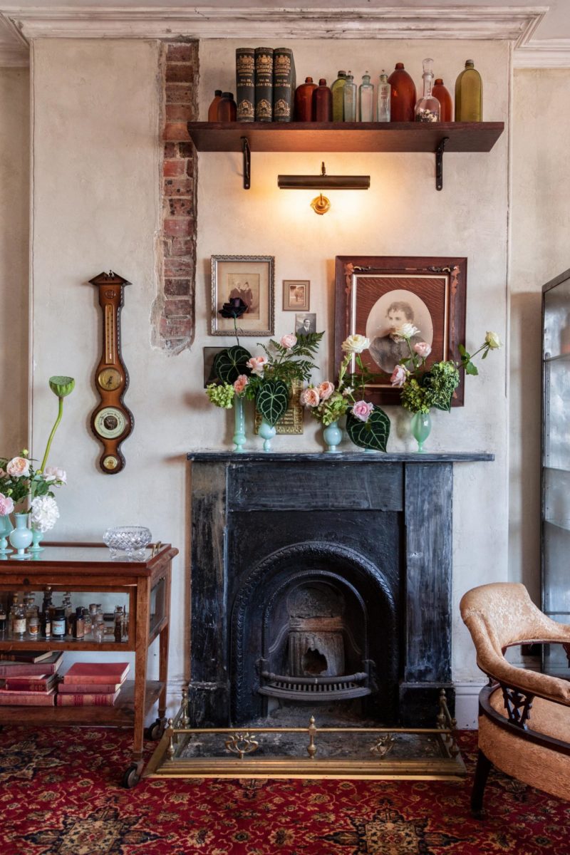 A fireplace in an old building, the mantle is decorating with several small green vases housing floral arrangements.